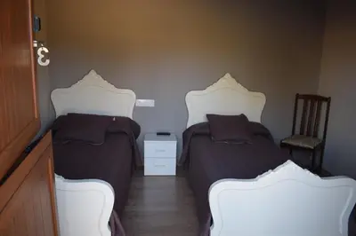 a bedroom with two beds and a chair at Pensión Albergue Los Caminantes in Ribadiso