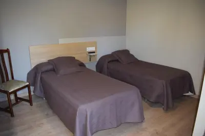 a hotel room with two beds and a chair at Pensión Albergue Los Caminantes in Ribadiso