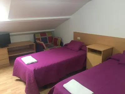 two beds in a small room with purple sheets at Hostal O Patron in Santiago de Compostela