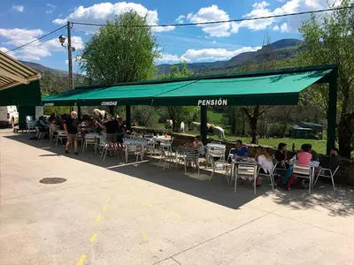 a group of people sitting in chairs under a green umbrella at Pensión Garcia in Tríacastela