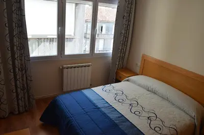 a bedroom with a bed with a blue blanket and a window at Del Peregrino in Arzúa