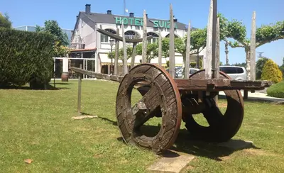 a wooden cart sitting in the grass in front of a house at Hotel Suiza in Arzúa
