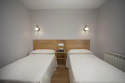 two beds in a room with a desk and lights at Hotel Novoa in Sarria