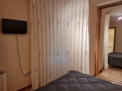a bedroom with white curtains and a tv and a bed at Apartamentos Rapadoira in Foz