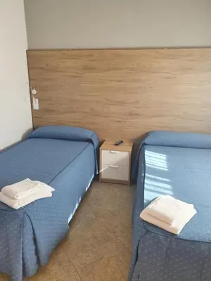 two beds in a room with blue sheets and white pillows at Pensión Portomiño in Portomarin