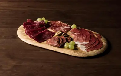 a plate of meat and grapes on a wooden board at Hotel Rural Las Montañas de Pumar in Besullo