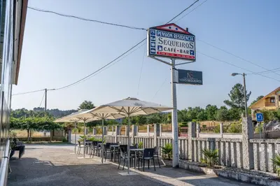 a sign for a restaurant with tables and umbrellas at Hostal Sequeiros in San Ciprián de Viñas