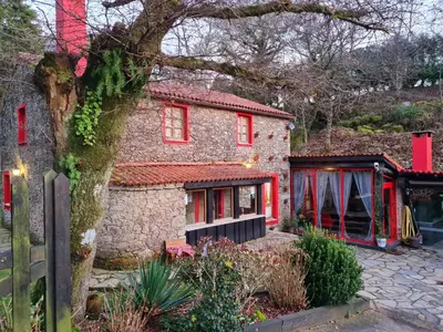 a stone house with red windows and a tree at A Pontiga I Casa Rural in Mezonzo