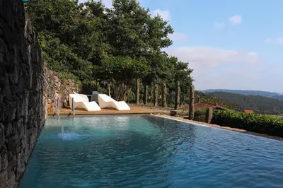 a swimming pool with two white lounge chairs next to a stone wall at Casa do Cebro Casa con piscina y jacuzzi privados in Santiago de Compostela