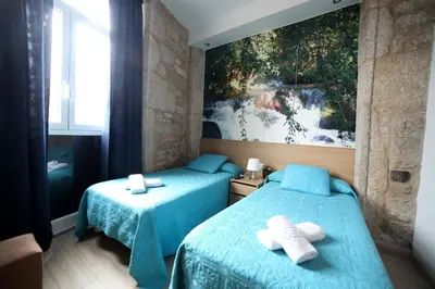 a bedroom with two beds with blue sheets and a painting at Pension Pardellas in Palas de Rei