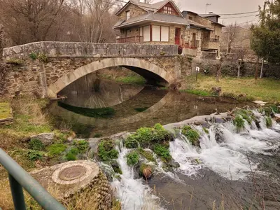 a stone bridge over a river with a waterfall at El Relax de Sanabria in Trefacio