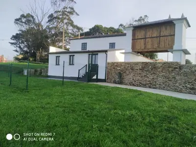 a white house with a stone wall and green grass at A Minguxaina in Ribadeo