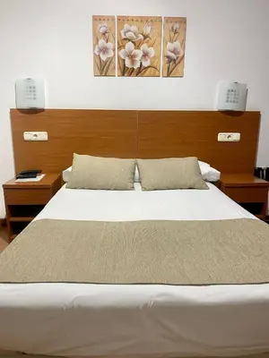 a bedroom with a large white bed with two lights at Pensión Residencia Fornos in Santiago de Compostela