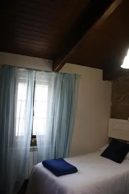 a bedroom with a bed and a window with blue curtains at A Casa da Meixida in Padrón