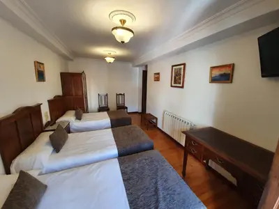 a room with two beds and a desk and a television at Hostal Giadás in Santiago de Compostela