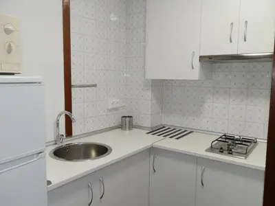 a white kitchen with a sink and a stove at Apartamentos Turisticos Beatriz in Perillo