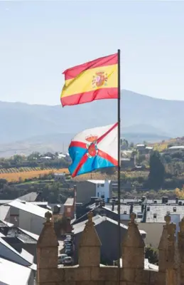 two flags are flying in front of a city at El Silencio de Galadhrim in Ponferrada