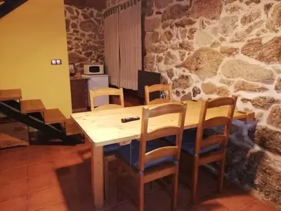 a table and chairs in a room with a stone wall at Apartamentos Rurales A Torre in Porqueira