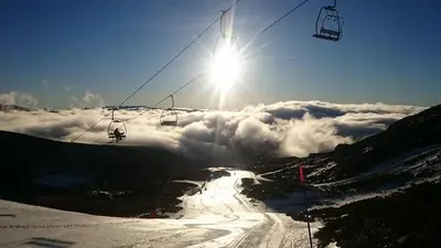 a ski lift on a mountain with the sun above the clouds at El cordal de laciana in Caboalles de Abajo