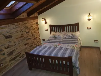 a bedroom with a wooden bed with a stone wall at Apartamentos Rurales Casa Carmen in Pola de Allande