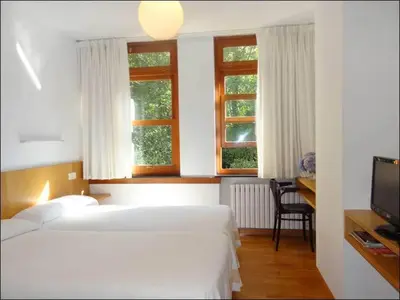 a bedroom with two beds and a desk and two windows at Hotel Restaurante Marroncín in Cangas del Narcea
