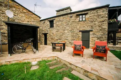 a patio with two chairs and a table in front of a stone building at Casa Calma Rural in Taramundi