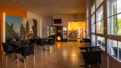 a restaurant with tables and chairs in a room with windows at Albergue Espiritu Xacobeo in O Pedrouzo