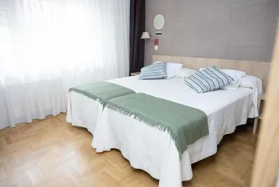 a bedroom with a bed with white and green sheets at Hotel El Molinón in Cangas del Narcea