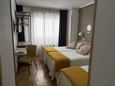 a hotel room with two beds and a desk and a mirror at Hotel El Molinón in Cangas del Narcea