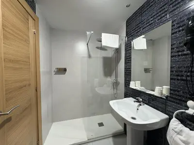 a white bathroom with a sink and a shower at Hotel El Molinón in Cangas del Narcea