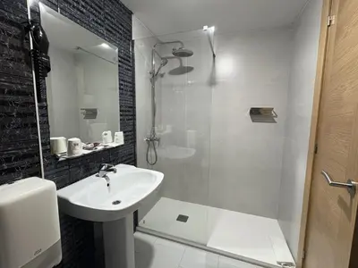 a white bathroom with a sink and a shower at Hotel El Molinón in Cangas del Narcea