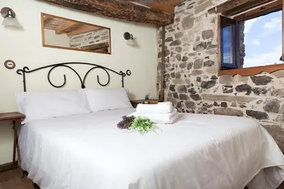 a white bed in a room with a stone wall at La Rosa del Agua in El Acebo de San Miguel