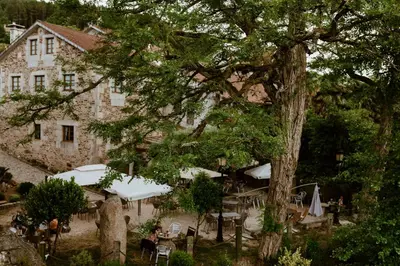 a tree in front of a building with tables and umbrellas at Casa da Capilla in Gres