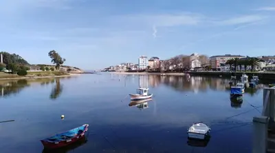 three boats are docked in a river with buildings at San Cibrao,belleza y tranquilidad. in San Ciprián
