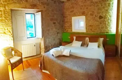 a bedroom with a bed and a chair and two windows at A Casa do Avó in Palas de Rei