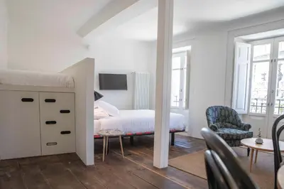 a white bedroom with a bed and a chair at Inferniño Apartments in Santiago de Compostela