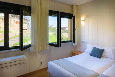 a bedroom with a bed and two windows at Hotel Alda Fogar do Mariñeiro in Ribadeo