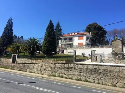 a house on the side of a road next to a stone wall at Albergue Mirador de Pedrouzo in O Pedrouzo
