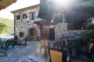 a patio with tables and chairs and an umbrella at Hotel Rural Valle de Ancares in Pereda de Ancares