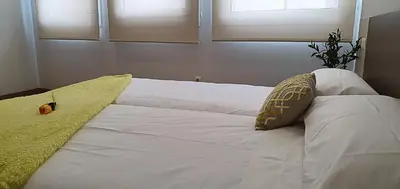 a white bed with a yellow pillow and two windows at Apartamentos Antares 2 in Milladoiro