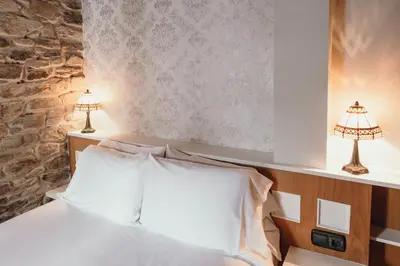 a bedroom with a bed with white sheets and two lamps at PR Campanas de San Juan in Santiago de Compostela