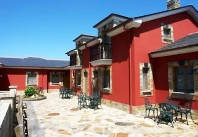 a red building with tables and chairs on a patio at Apartamentos Porcia in Tapia de Casariego
