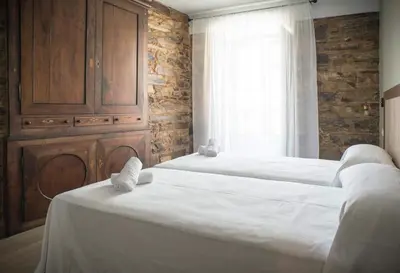 two beds in a bedroom with a brick wall at Hotel portico in Fonsagrada