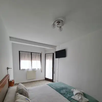 a white bedroom with a bed and a television at Apartamentos O Cargadeiro Ribadeo in Ribadeo