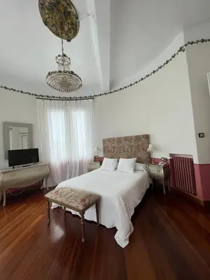 a bedroom with a large white bed and a chandelier at Hotel Palacete Peñalba in Castropol