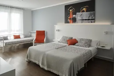 a white bedroom with a bed and a chair at Xabarin Rooms in Abadín