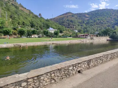a river with a stone wall and people swimming in it at Hostal Cruce in Villafranca del Bierzo