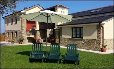 two chairs and an umbrella in front of a house at Apartamentos Rurales Casanova in Tapia de Casariego