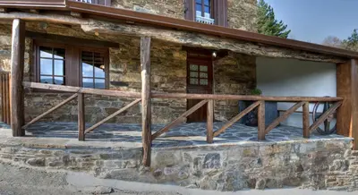 a front porch of a stone house with a wooden rail at Apartamentos A Casa Nova in A Pontenova