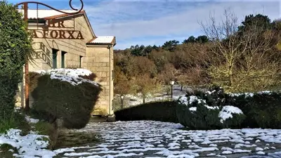 a house with snow on the ground in front of it at Hotel A Forxa Cafetería Restaurante in Carballeira